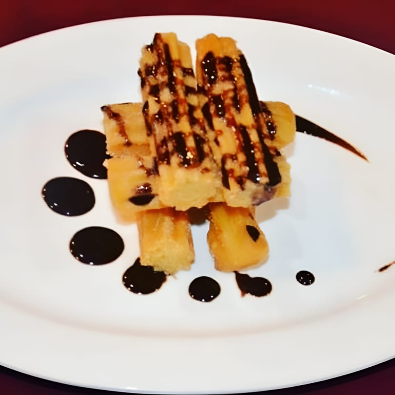 Golden churros drizzled with dark chocolate sauce, artfully arranged on a white plate.