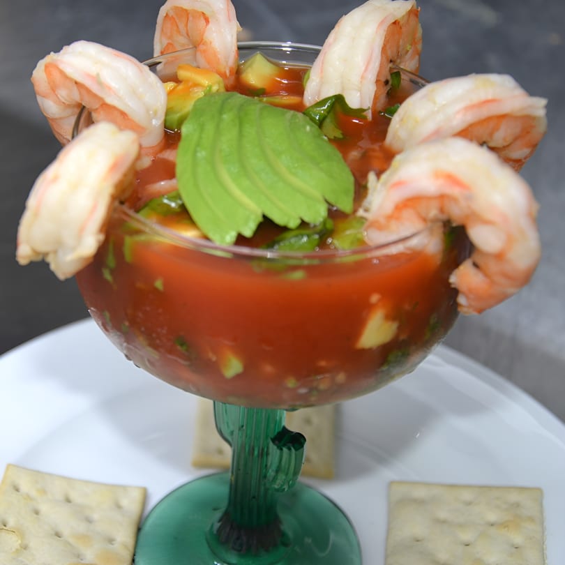 Avocados Mexican Grill's shrimp cocktail in a cactus-stemmed glass, garnished with avocado slices and crackers.